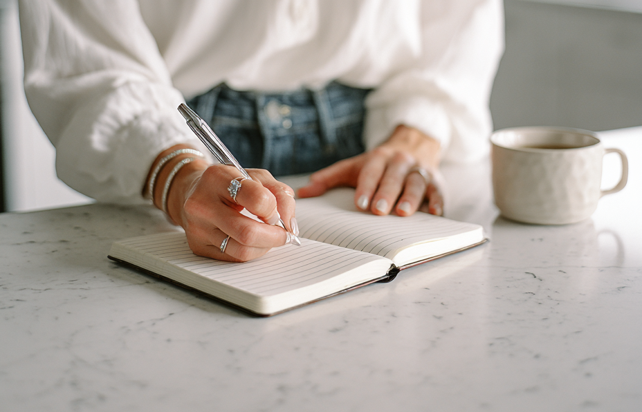 Woman writing in a notebook with a cup of coffee on a marble surface